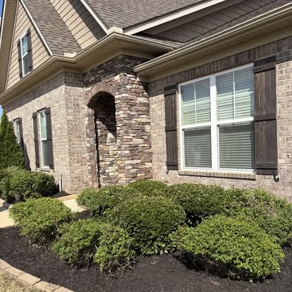 Stone column entryway with neatly trimmed shrubs and clean foundation bed